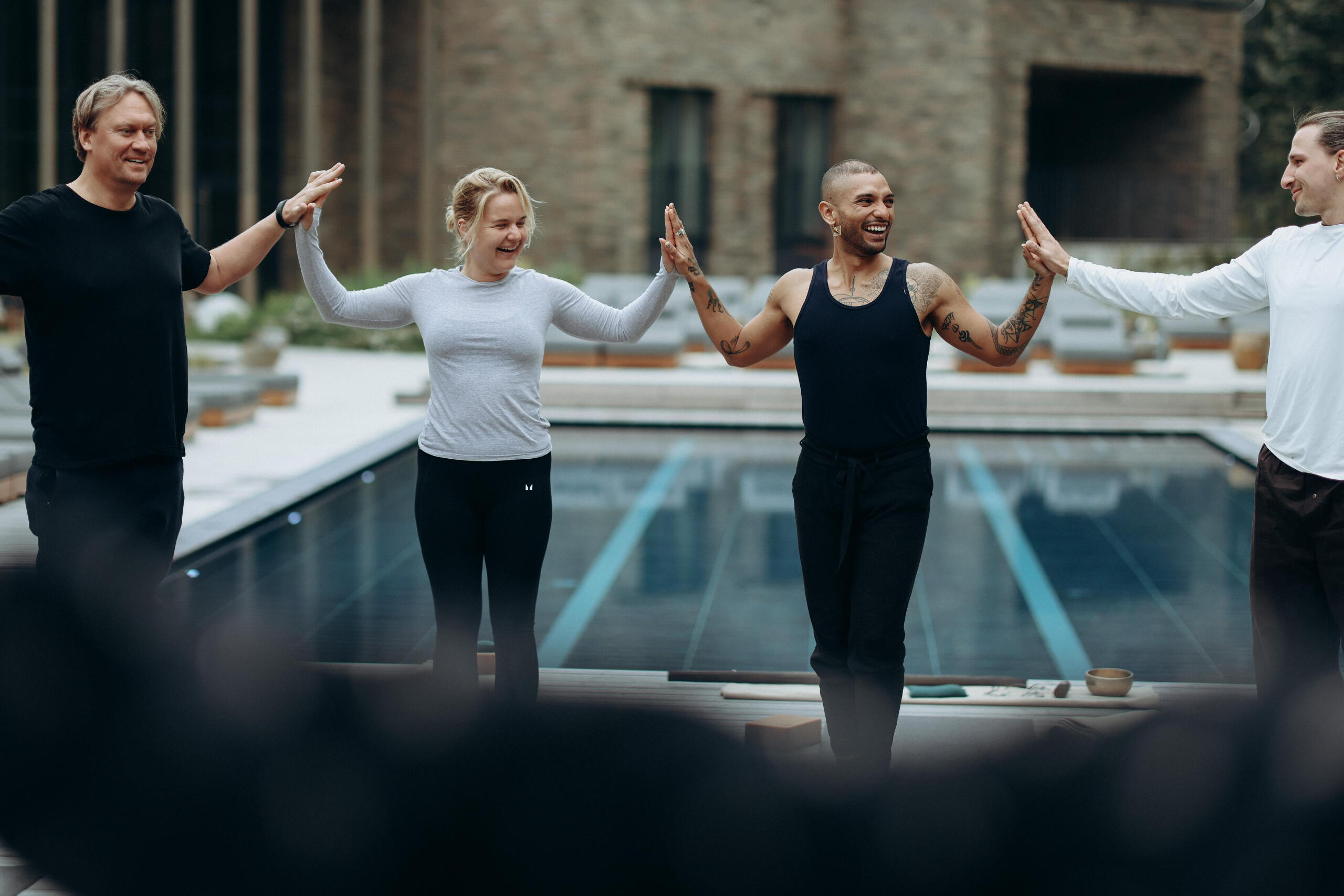 Free Lopez leading a daytime connection ritual by a pool, with participants standing in a circle and touching palms, fostering unity, trust, and shared presence.